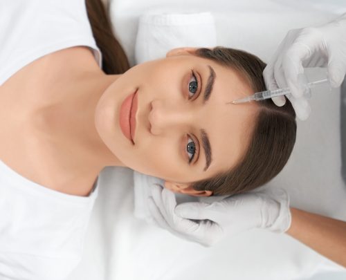 Top view portrait of cute young woman lying on procedure for improvements face skin in beautician. Concept of procedure injection anti-aging skin with professional cosmetics.